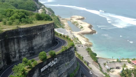 un automóvil viaja por la carretera en forma de s que atraviesa la colina, y la playa melastic de uluwatu bali se puede ver desde la cima de la colina