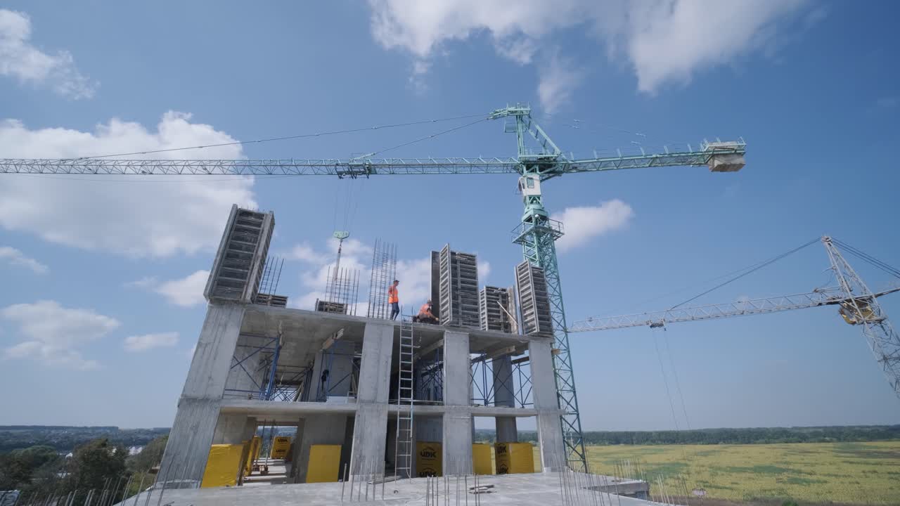 las grúas de torre trabajan en la construcción de edificios residenciales de ladrillo contra el fondo de un cielo azul.