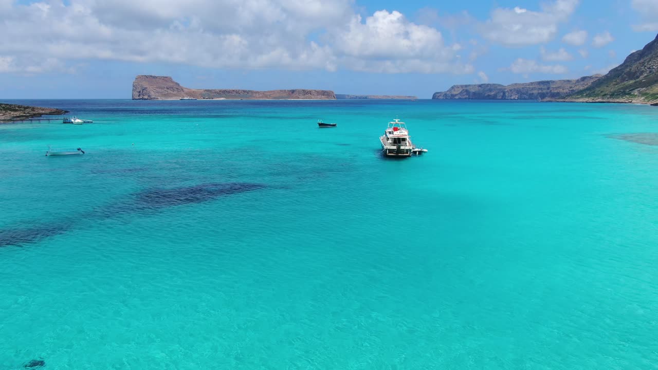 Balos Beach turquoise waters in Crete Greece with tourist transport ship and it's dingy boat attached, Aerial flyover reveal shot