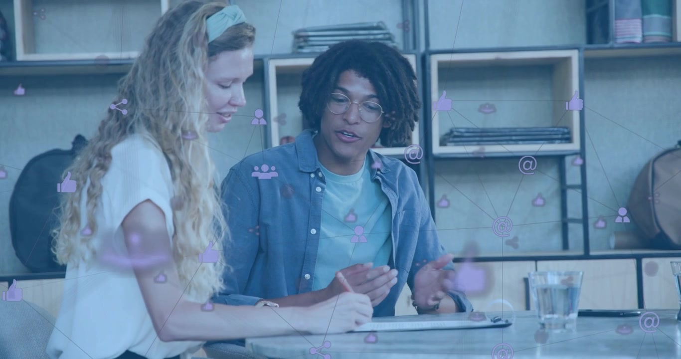 Man explaining ideas and woman writing on paper with floating icons guiding office brainstorming