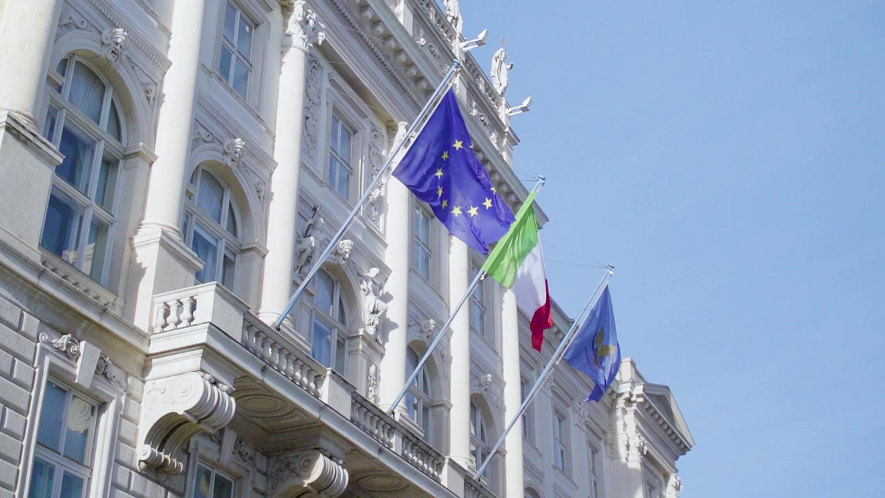 Ripresa al rallentatore delle bandiere dell'Unione Europea e dell'Italia che sventolano su un edificio in Piazza Unità d'Italia a Trieste, Italia