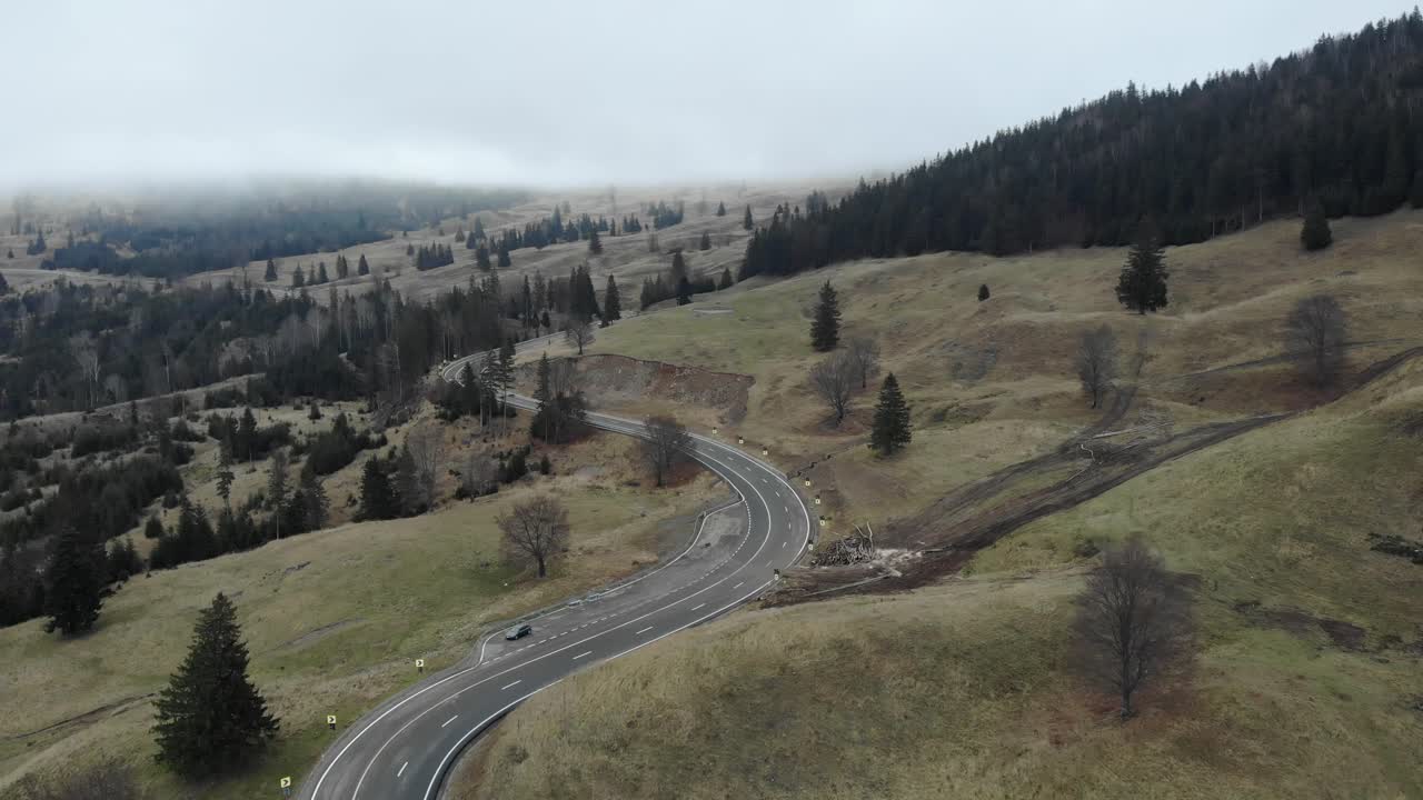 carretera en las colinas inclinadas con árboles de bosque de coníferas contra el cielo cambiante
