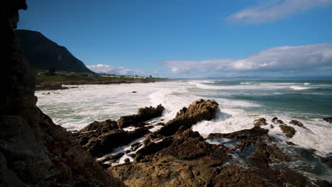 View-from-rocky-shoreline-as-waves-crash-onto-beach-in-Voëlklip,-Hermanus