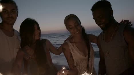 multi-ethnic couples celebrating with sparklers at beach at night