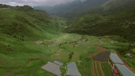 Aerial-view-of-lush-valley-in-Sapa,-Vietnam,-featuring-terraced-fields,-greenhouses,-and-rolling-hills