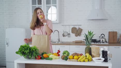 happy housewife with fresh fruit and vegetables in the kitchen. young woman unpack organic food from paper bag at home. vertical video