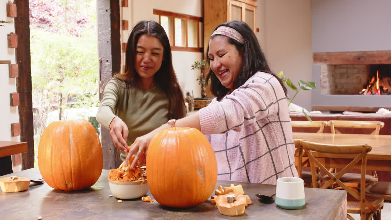Multiracial grandmother and young woman carving pumpkins in cozy kitchen, at home, halloween time
