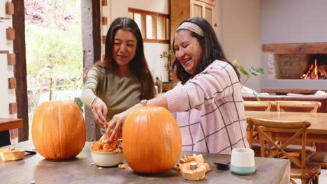 multiracial grandmother and young woman carving pumpkins in cozy kitchen, at home, halloween time