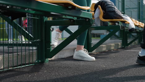 side leg view of an athlete in sneakers and joggers entering a sports court, passing a bench with a jacket laid on it, highlighting the beginning of a training session