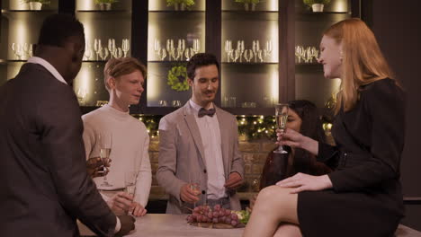 group of friends dressed in elegant clothes celebrating the new year's party, they stand around the bar counter while toasting and drinking champagne