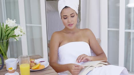 woman in bath towel reading book at table