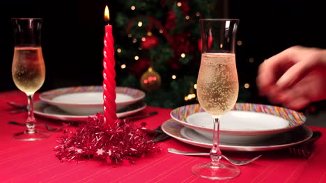 mano de mujer poniendo flauta de champán en mesa roja puesta para navidad a cámara lenta