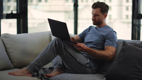 Beard-man-working-remotely-home.-Male-person-sitting-on-couch-with-computer.