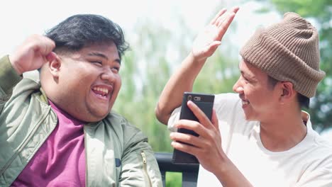 two young asian college students using tablet and smartphone and giving high five to each other celebrating victory