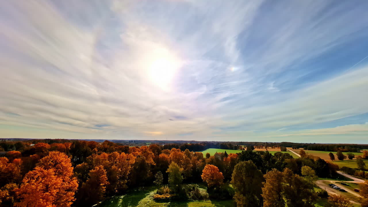 A circular halo surrounds the sun above a colorful autumn forest and open countryside. Europe