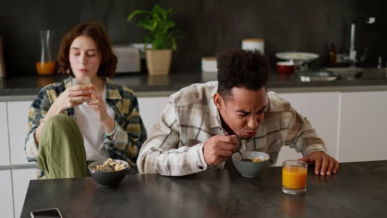 흑인 갈색 남자는 아침 식사 중에 주스와 함께 시리얼을 좋아하지 않았고, 아침 식사 동안 그의 젊은 성인 갈색 여자 친구와 함께 그의 접시에 바로 습니다.