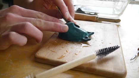 An-artist-using-wet-sandpaper-while-sculpting-and-polishing-his-polymer-clay-mask-figurine-in-an-art-studio-with-tools-and-brushes