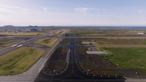 iceland international airport with distant airplane taking off on sunny day, aerial