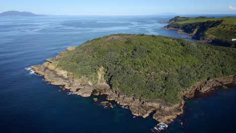 antena circular sobre la isla de las cabras, vegetación próspera y costa rocosa que revela el vasto y tranquilo océano que lo rodea, nueva zelanda