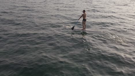 Aerial-drone-static-shot-of-man-exercising-on-a-sup-paddle-board-in-turquoise-tropical-clear-waters,-in-Thailand