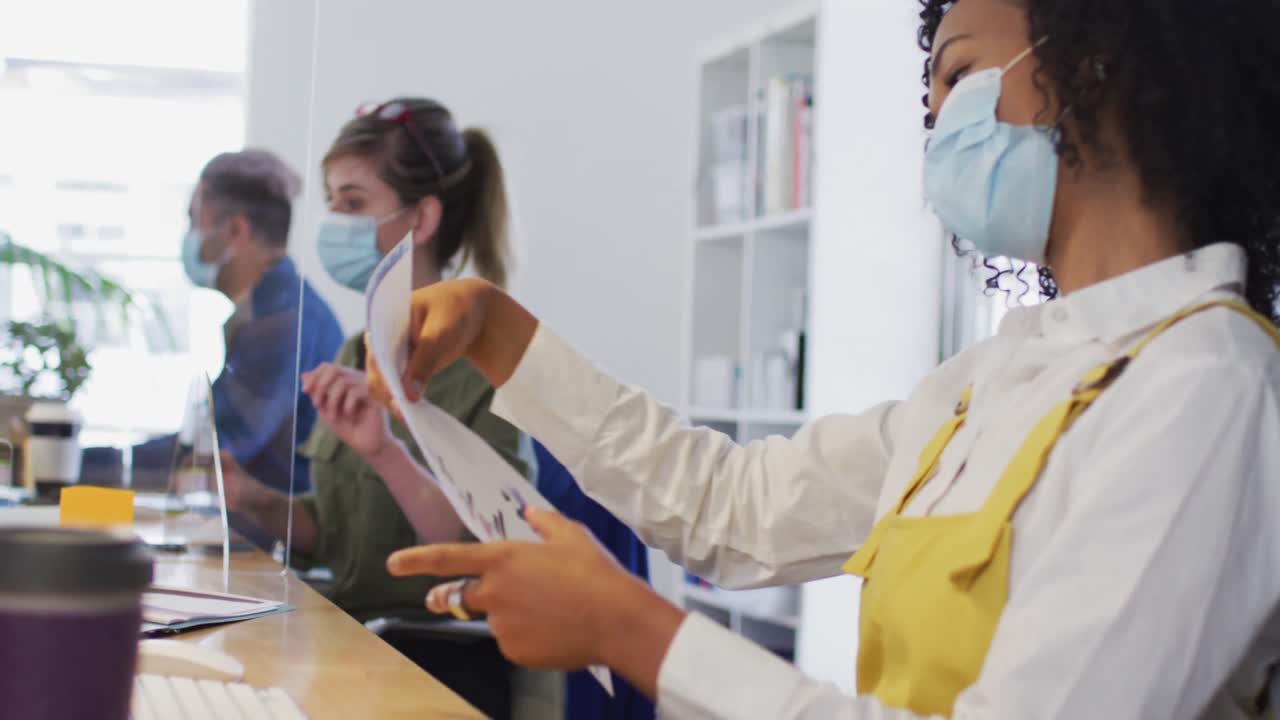 Woman wearing face mask passing a document to her colleague at office