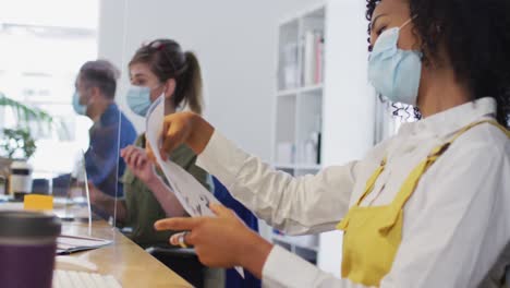 woman wearing face mask passing a document to her colleague at office