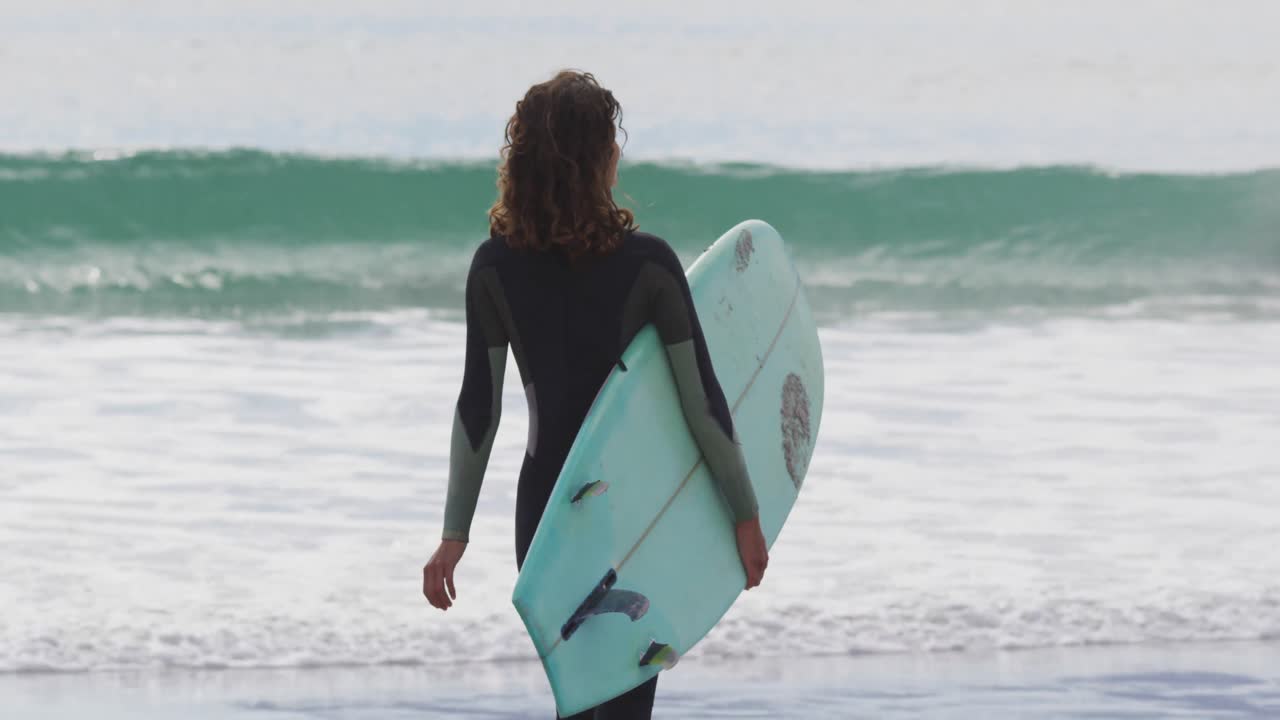 Di spalle, donna di etnia mista che cammina in mare con una tavola da surf.