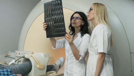 two doctors discussing the examination results of mri scanning for young male patient, showing the snapshot with images, observing and analyzing mri scan in modern clinic beside modern closed-type mri