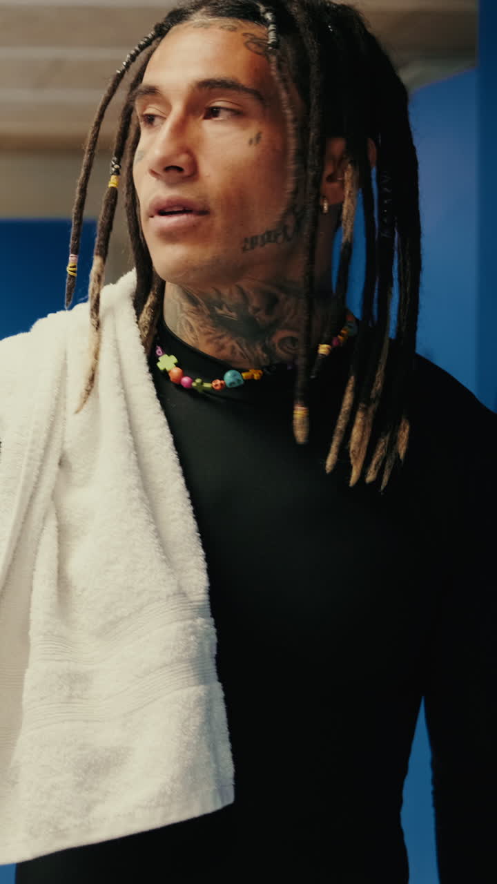 Uomo con dreadlock e tatuaggi in piedi in uno spogliatoio