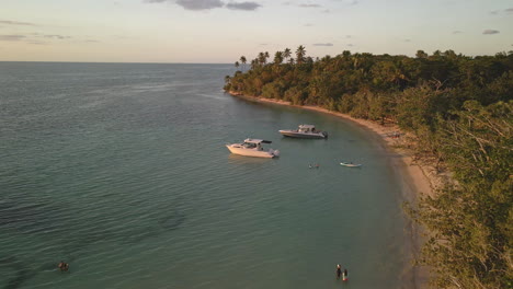 Flying-drone-over-boats-in-crystal-clear-blue-waters-during-sunset