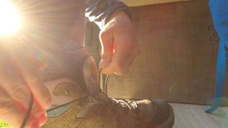 Young-man-tightens-knot-on-hiking-shoe,-preparing-for-a-hike,-static-shot