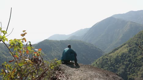 Isolierter-Junger-Mann-Auf-Bergspitze-Mit-Grünen-Wäldern-Und-Nebelblauem-Himmel-Am-Morgen-Aus-Einem-Flachen-Winkelvideo-Wird-Beim-Mawryngkhang-Trek-Meghalaya-Indien-Aufgenommen