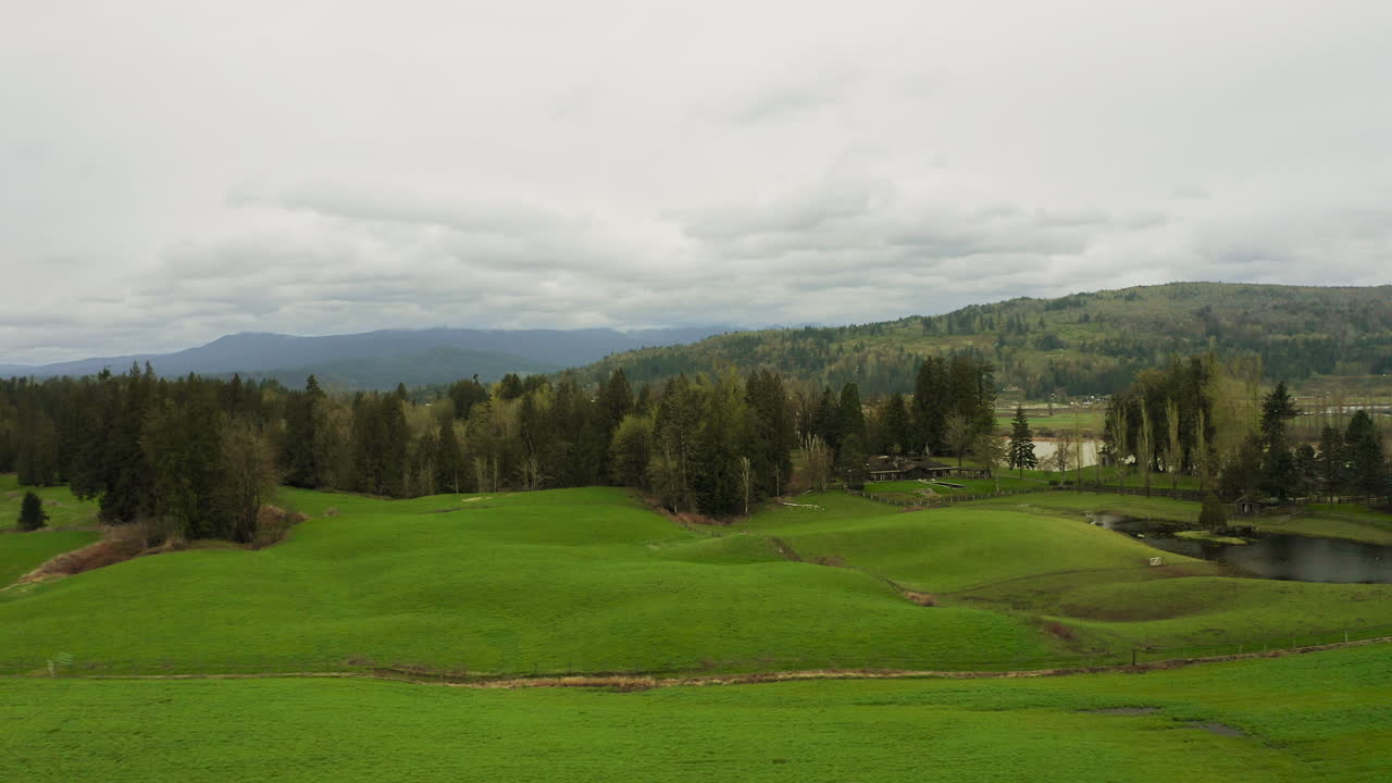 ⁇ 어져있는 나무와 농장 건물과 함께 봄에 구름진 하늘과 함께 넓은 느리게 움직이는 강 근처의 녹색 잔디 농지의 부드러운 공중  ⁇