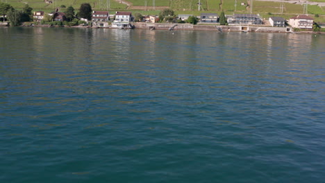 Drone-flying-over-Geneva-lake,-tilting-up-and-flying-over-beautiful-lakeside-houses