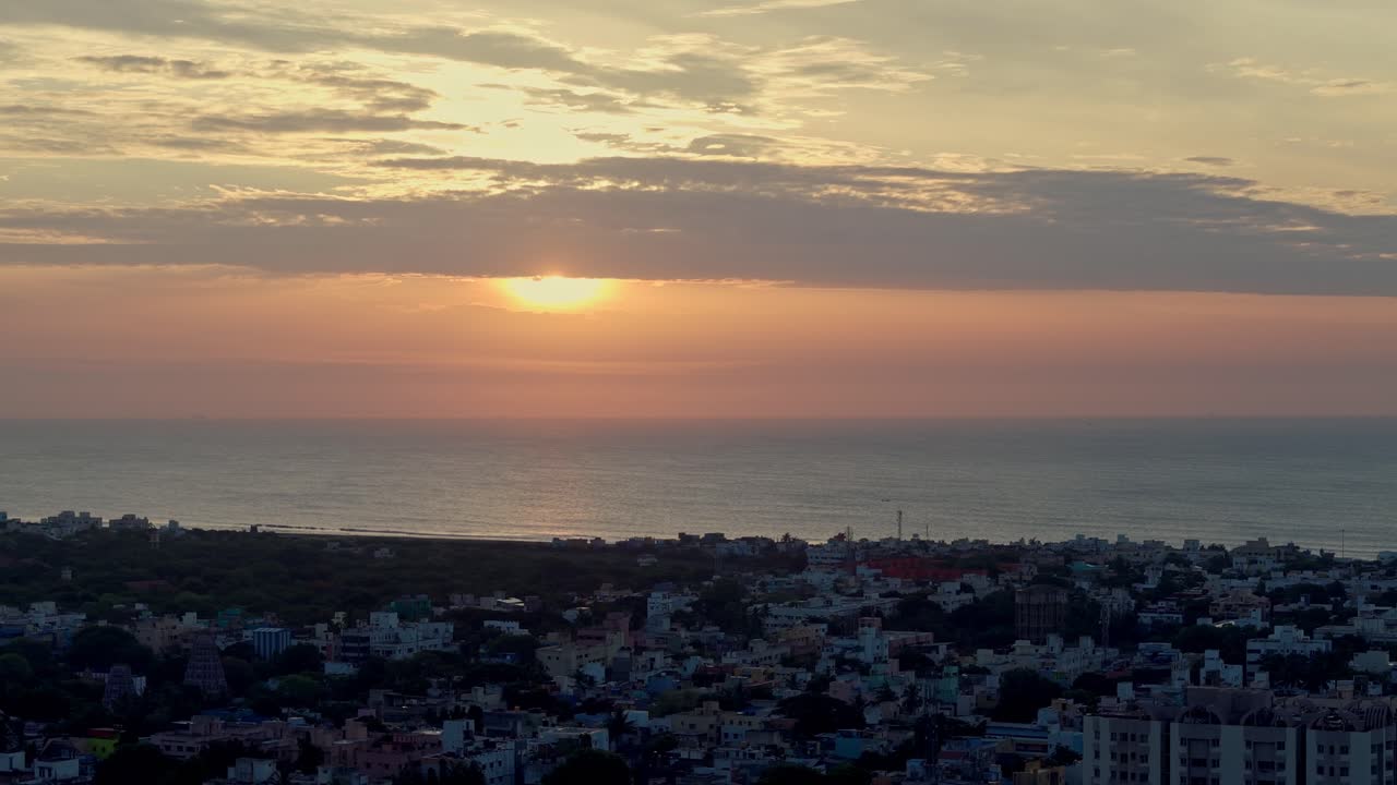 Aerial shot of thick layer of clouds blocking sunlight to fall on city over an ocean.