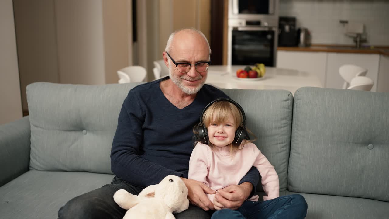 retrato de una niña pequeña con auriculares con su abuelo mientras está sentada en el sofá