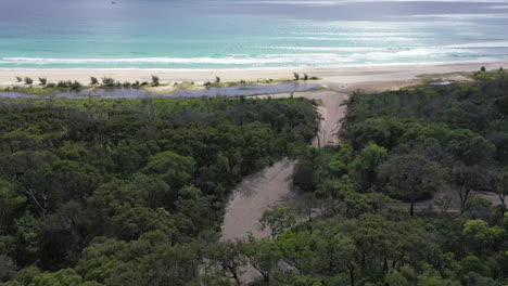 Tracking-aerial-follows-truck-as-it-turns-from-forest-road-to-beach