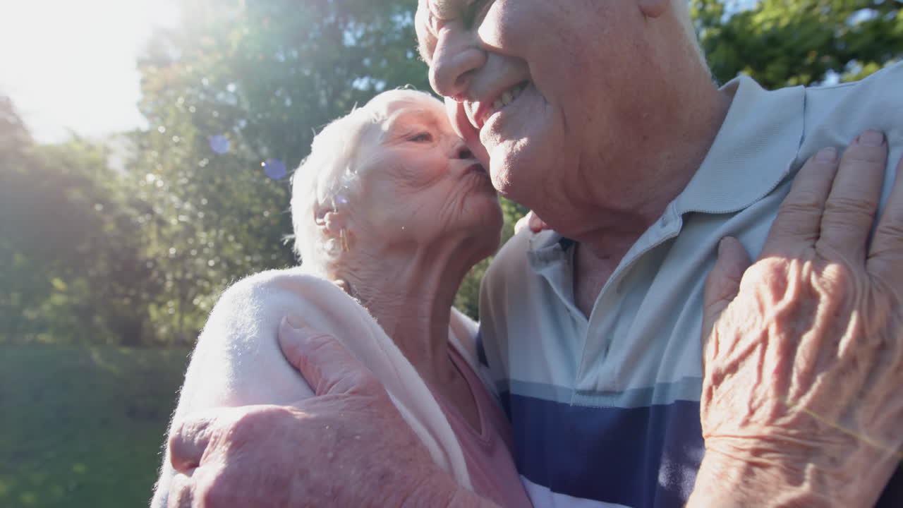 una feliz pareja caucásica se abraza y besa en un jardín soleado, en cámara lenta.