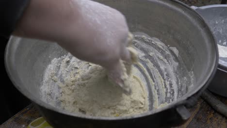 kneaded dough in a black cauldron. the dough is soft and covered with flour, while it is kneaded with one hand by a chef in nature. the cauldron is on a chopper above a table.
