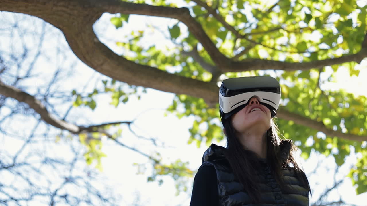joven de cabello oscuro en un cálido chaleco negro caminando en el parque de otoño temprano