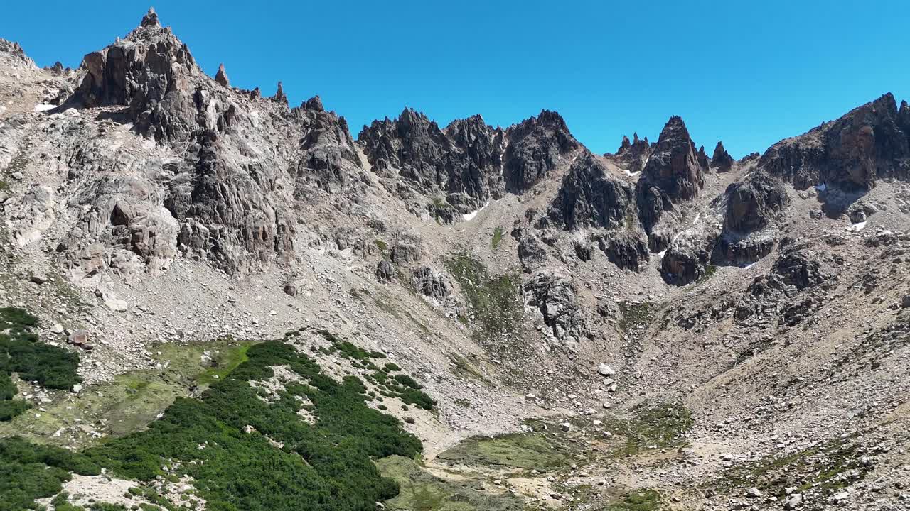 Panoramica aerea fluida sulla Laguna Tonchek in Patagonia, Argentina. L'inquadratura si sposta da un letto di fiume asciutto verso aspre cime montuose sotto una luce solare intensa e cieli sereni