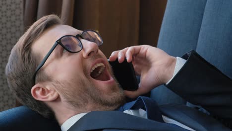 Close Up Cheerful Businessman Talking on the Phone During a Break. Cheerful businessman talking on the phone during a break. Close up. Businessman relaxing on sofa in office as business concept
