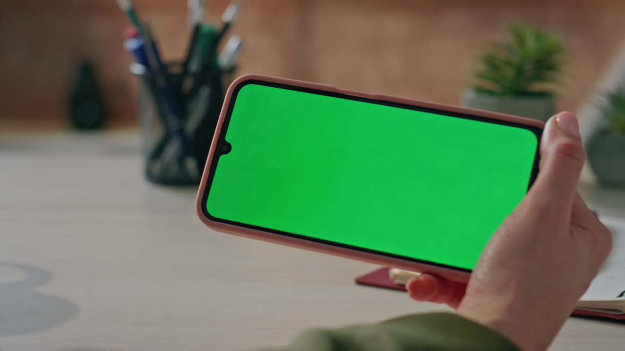 Woman hands holding chroma key cellphone at workplace close up. Manager watching