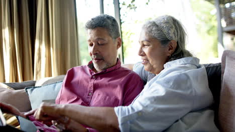 happy diverse senior couple sitting on couch and using tablet for online shopping at home