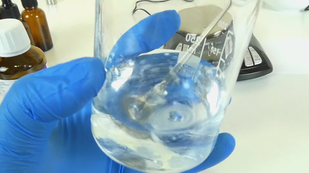 A video showcasing the process of shaking a clear, transparent serum in a glass beaker in a professional cosmetic laboratory.