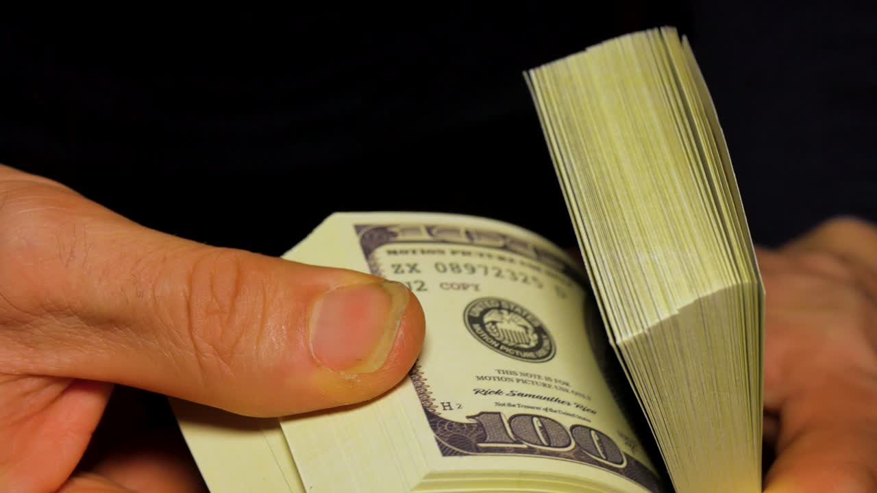 A man playing with a wad of money. There are one hundred dolars bills.