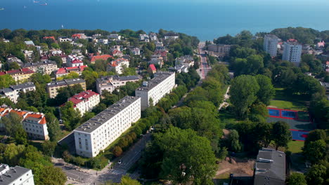 aerial backwards shot showing beautiful city of gdynia with park and trees and blue baltic sea in background