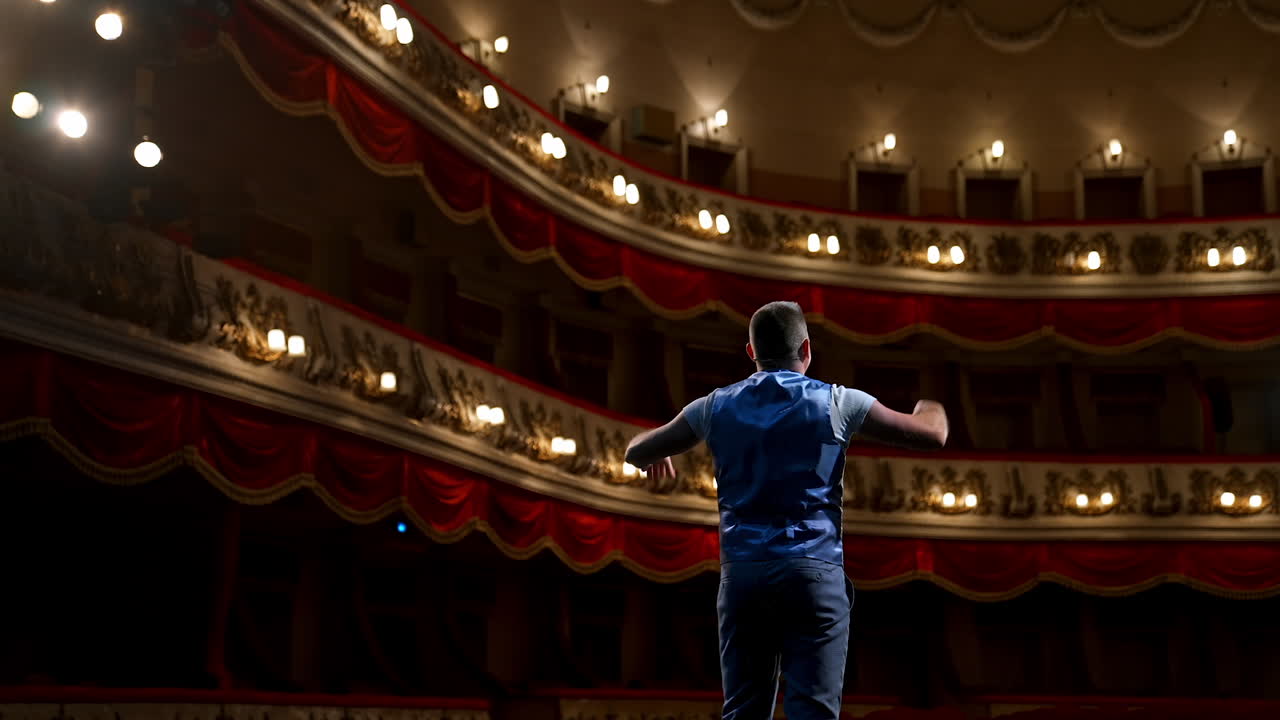 Actor bowing on theatrical stage. Man is standing on the scene of the classical theater and acting his role during the rehearsal before the empty hall. Back view.