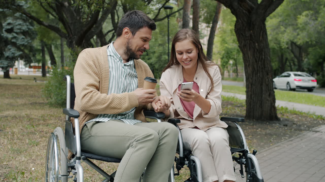 Couple in Wheelchairs Enjoying Coffee and a Smartphone in the Park