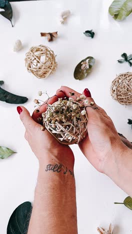 hands holding a small wicker sphere with dried flowers